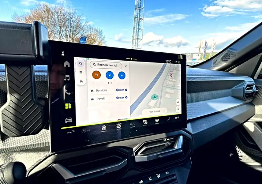 Vue intérieure du tableau de bord du Dacia Duster noir 2026, avec écran tactile GPS et commandes climatisation visibles.