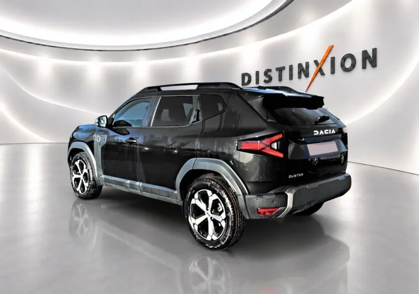 Dacia Duster noir vue 3/4 arrière droit en intérieur, avec jantes alu et barres de toit visibles.