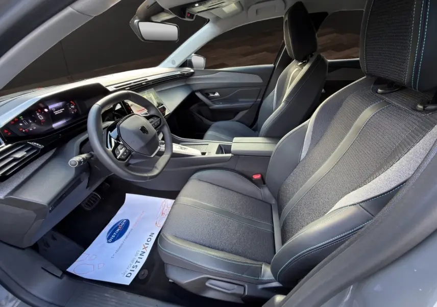 Vue intérieure côté conducteur de la Peugeot 308 Hybrid 145 e-DCS6 Allure 2025 avec sièges tissu et cuir gris foncé.