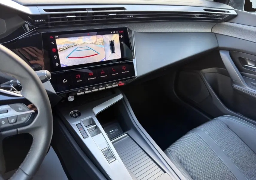Intérieur de la Peugeot 308 Hybrid 145 e-DCS6 Allure 2025, vue côté passager avec écran tactile et console centrale grise.