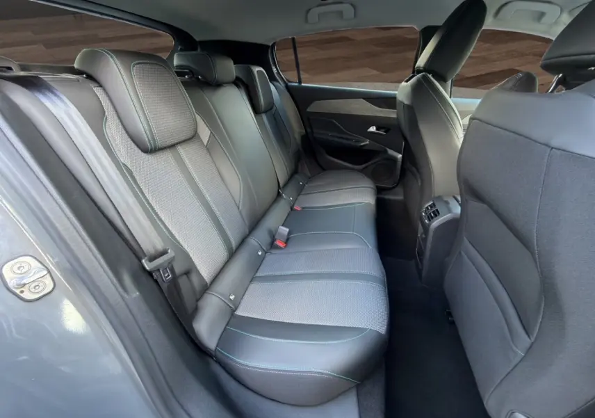 Vue intérieure arrière côté gauche de la Peugeot 308 Hybrid 145 Allure, sièges gris foncé en cuir et tissu avec surpiqûres bleues.