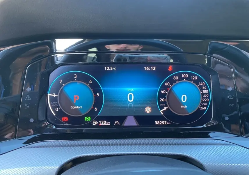 Vue rapprochée du tableau de bord numérique bleu de la Volkswagen Golf VIII noire, affichant vitesse et régime moteur à l'arrêt.