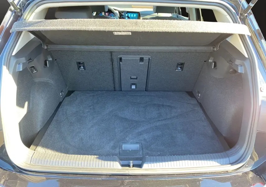 Coffre ouvert vu de l'arrière d'une Volkswagen Golf VIII noire, avec habillage intérieur gris et tablette de séparation.