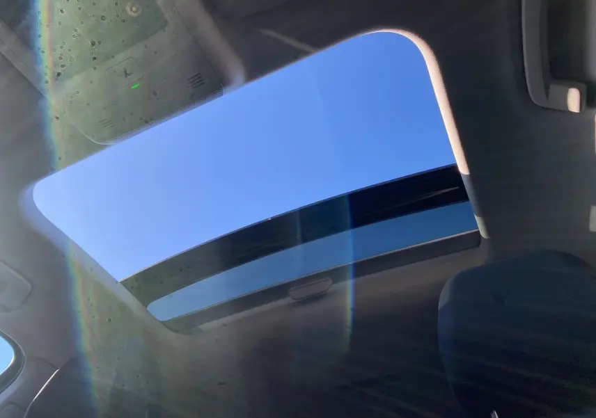 Vue intérieure du toit panoramique ouvert de la Volkswagen Golf VIII noire, laissant apparaître un ciel bleu lumineux.