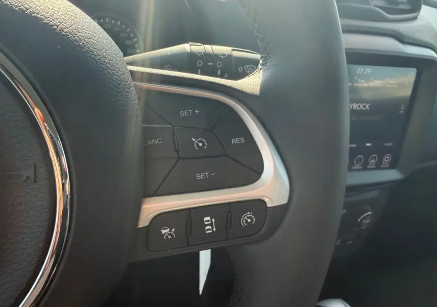 Gros plan sur le volant noir de la Jeep Renegade 2023, montrant les commandes du régulateur de vitesse et l'écran tactile en arrière-plan.