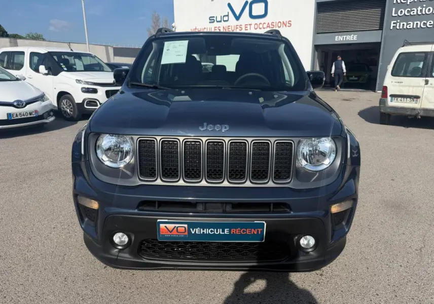 Vue frontale d'un Jeep Renegade bleu 2023 avec calandre à sept fentes et phares ronds, stationné devant un concessionnaire.