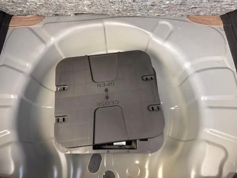 Vue plongeante sur le coffre ouvert d'une Renault Clio V noire 2025, montrant le compartiment de rangement sous la moquette.