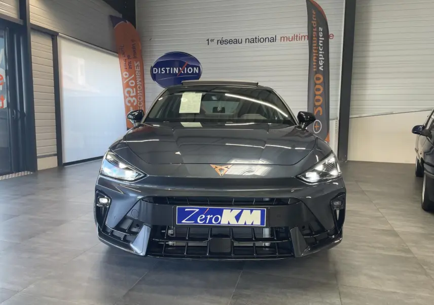 Vue frontale d'une CUPRA Leon gris magnétique avec logo cuivré et phares LED allumés en showroom.