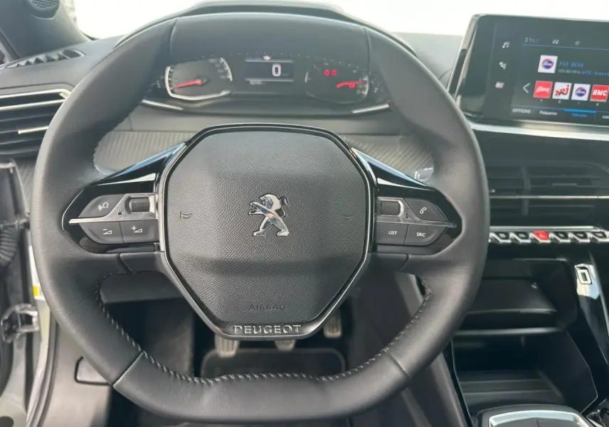 Volant compact en cuir noir avec logo Peugeot, tableau de bord numérique et écran tactile central du Peugeot 2008 gris clair.