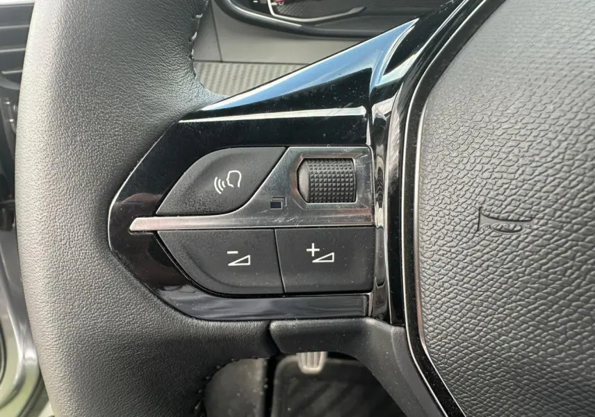 Gros plan sur les commandes multimédia à gauche du volant noir du Peugeot 2008 gris clair de 2022.