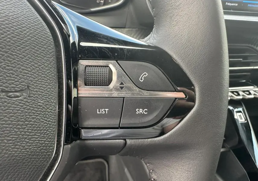 Gros plan sur les commandes multimédia noires à gauche du volant cuir du Peugeot 2008 gris clair 2022.