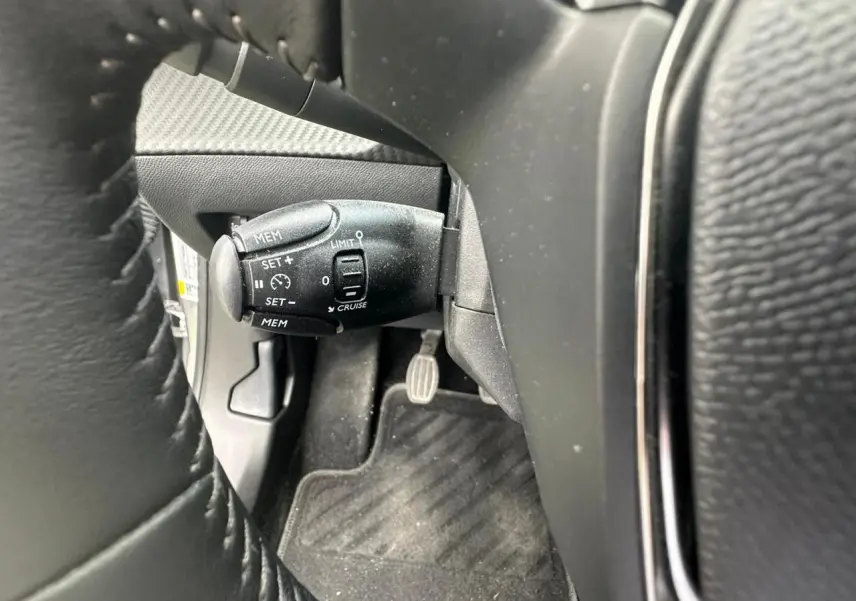 Gros plan sur la commande de régulateur de vitesse noire à gauche du volant cuir du Peugeot 2008 gris clair.
