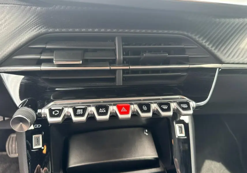 Gros plan sur la console centrale noire du Peugeot 2008 II avec boutons argentés et rouge d'alerte, prise USB visible.