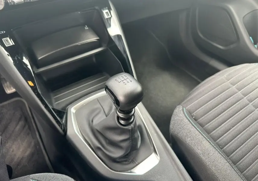 Le levier de vitesses manuel noir et la console centrale brillante d'une Peugeot 2008 gris clair, vue côté droit intérieur.