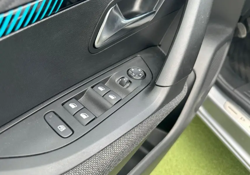 Détail de la commande des vitres électriques côté conducteur d'une Peugeot 2008 gris clair, avec insert bleu sur la porte.