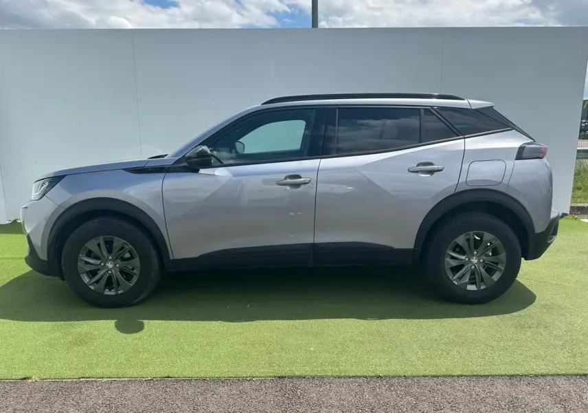 Profil côté gauche du Peugeot 2008 gris clair de 2022 avec jantes alliage et barres de toit noires.