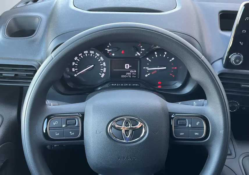 Vue rapprochée du volant noir Toyota PROACE CITY 2023 avec commandes intégrées et tableau de bord digital.