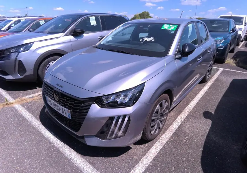 Peugeot 208 gris clair vue 3/4 avant droit, calandre noire et feux LED à signature verticale, stationnée en extérieur.