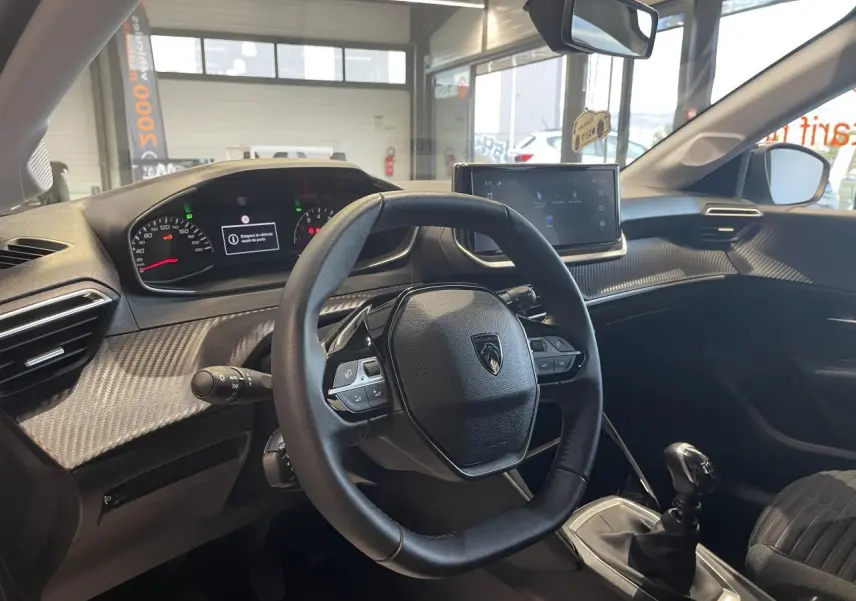 Intérieur de la Peugeot 208 2024 vue côté conducteur, volant cuir, tableau de bord et levier de vitesses manuelle.