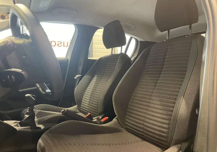 Vue intérieure côté conducteur montrant les sièges avant en tissu noir avec surpiqûres et levier de vitesses manuel.