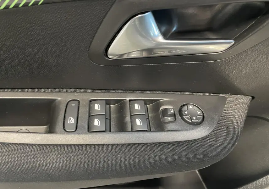 Détail des commandes de lève-vitres et réglage des rétroviseurs sur la porte avant gauche d'une Peugeot 208 gris clair 2024.