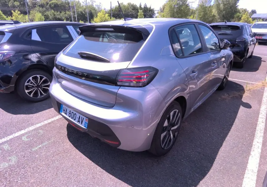 Vue 3/4 arrière droite d'une Peugeot 208 gris clair avec becquet noir brillant et feux arrière à LED en forme de griffes.