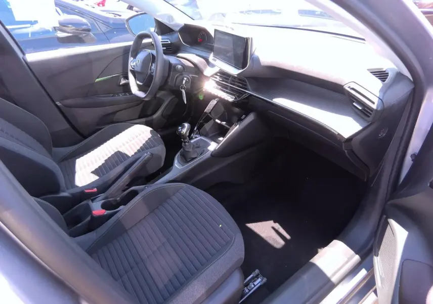 Intérieur avant droit de la Peugeot 208 2024 avec sièges tissu gris et console centrale équipée d’une boîte manuelle.