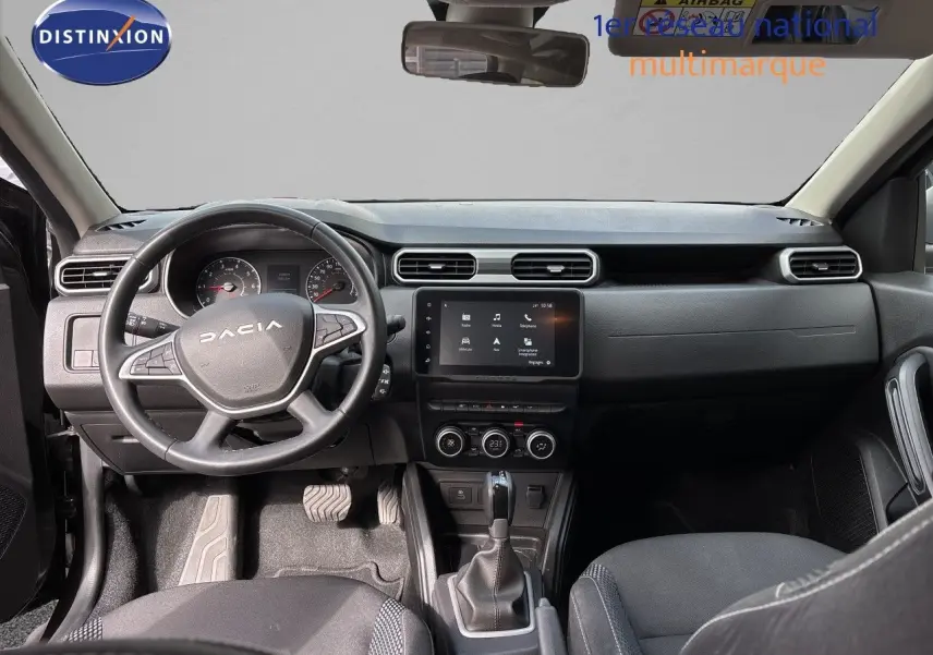 Vue intérieure avant du Dacia Duster 2024 noir, montrant le tableau de bord avec écran tactile et volant multifonction.