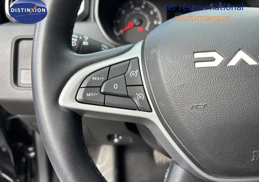 Gros plan sur le volant noir du Dacia Duster 2024 avec commandes de régulateur de vitesse visibles à gauche.