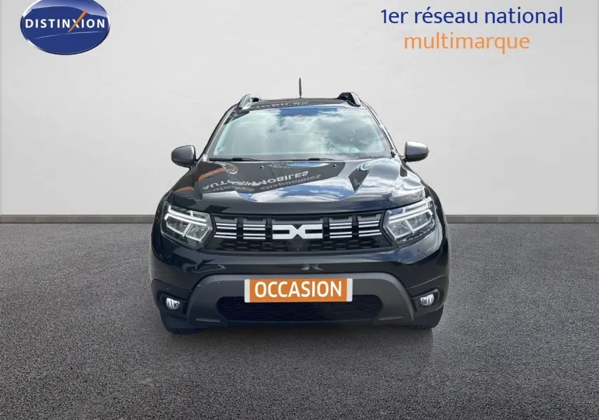 Vue frontale d'un Dacia Duster noir 2024 avec calandre distinctive et feux LED allumés sur fond neutre.