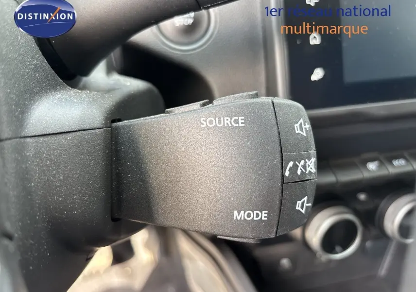 Gros plan sur la commande au volant du Dacia Duster noir 2024, avec boutons source, mode et contrôle audio visibles.