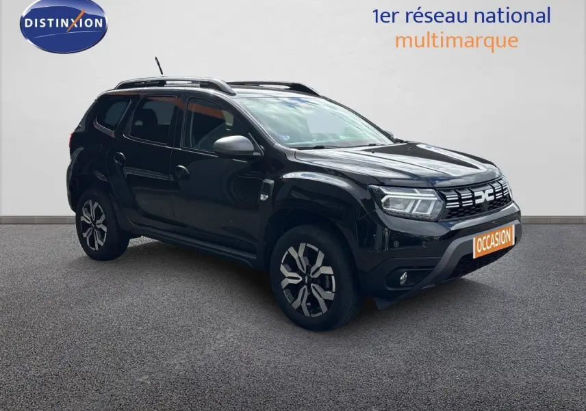 Dacia Duster noir en 3/4 avant droit, avec jantes bi-ton et barres de toit visibles sur fond neutre.