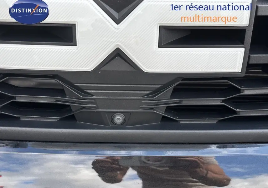 Gros plan sur la calandre noire du Dacia Duster 2024 avec caméra frontale intégrée sous le logo.