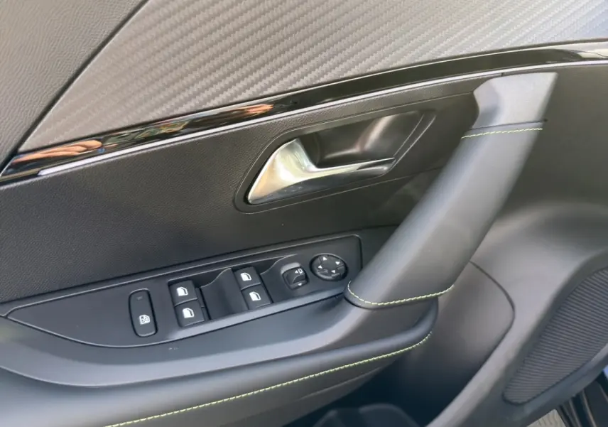 Gros plan sur la porte intérieure côté conducteur du Peugeot 2008 Hybrid 145 e-DCS6 GT, avec surpiqûres vertes et commandes électriques.