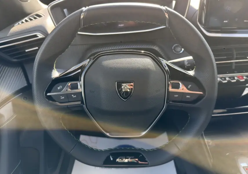 Volant cuir noir multifonctions de Peugeot 2008 Hybrid 145 e-DCS6 GT, vue frontale centrée sur le logo et commandes intégrées.