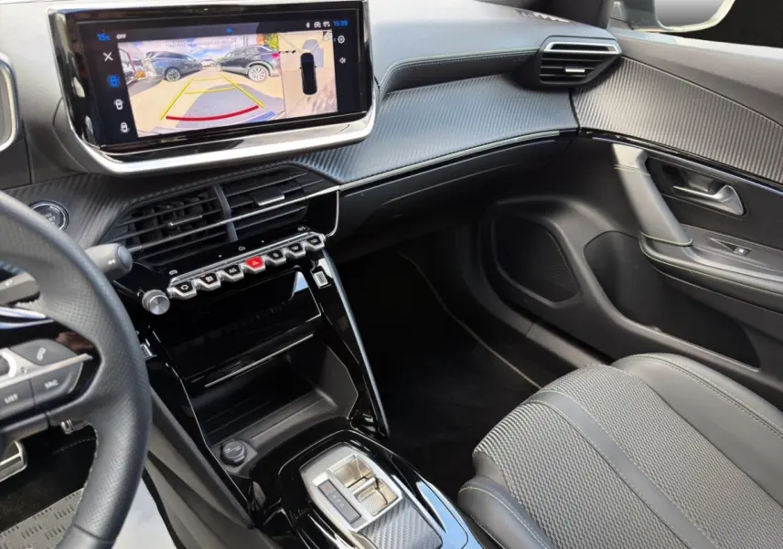 Vue intérieure côté passager du tableau de bord et console centrale noire avec écran tactile et volant cuir partiel du Peugeot 2008 Hybrid 145 GT.