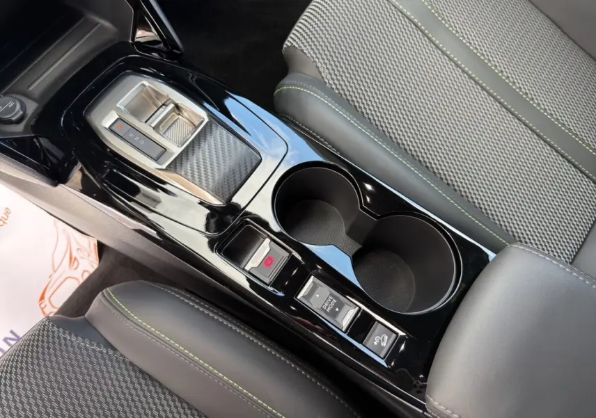 Vue rapprochée de la console centrale noire brillante avec levier de vitesses et sièges gris à surpiqûres vertes du Peugeot 2008 Hybrid 145.