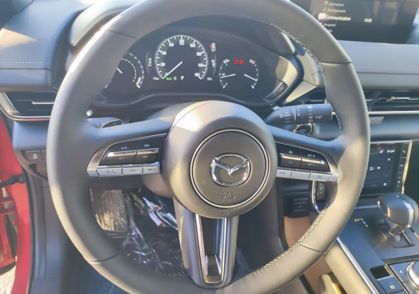 Vue rapprochée du volant noir de la Mazda MX-30 rouge métal 2023 avec commandes intégrées et tableau de bord numérique.