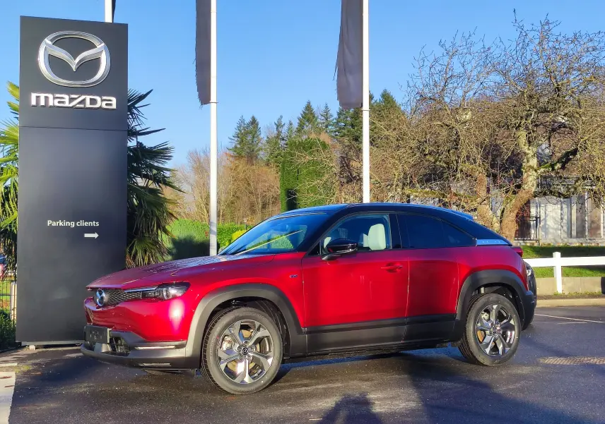 Vue latérale droite d'un Mazda MX-30 rouge métal 2023, soulignant ses jantes et son toit noir contrastant.