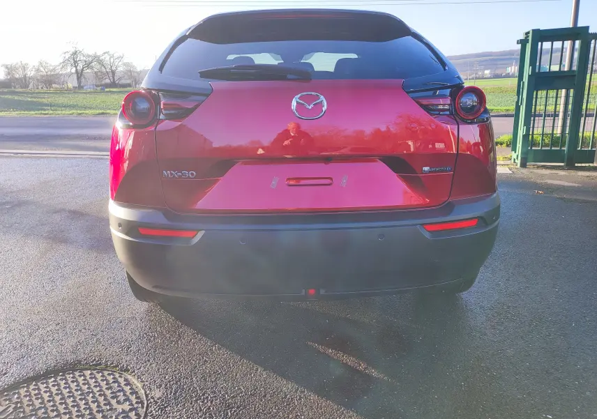 Vue arrière d'une Mazda MX-30 rouge métal 2023 avec feux ronds et logo Mazda bien visibles.