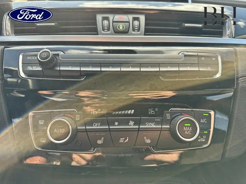 Tableau de bord noir brillant avec commandes climatisation et audio d'une BMW X1 xDrive25eA 2021 vue de face.