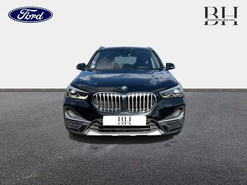 Vue frontale d'un BMW X1 xDrive25eA 220ch xLine 2021 en noir saphir avec calandre imposante et phares LED allumés.