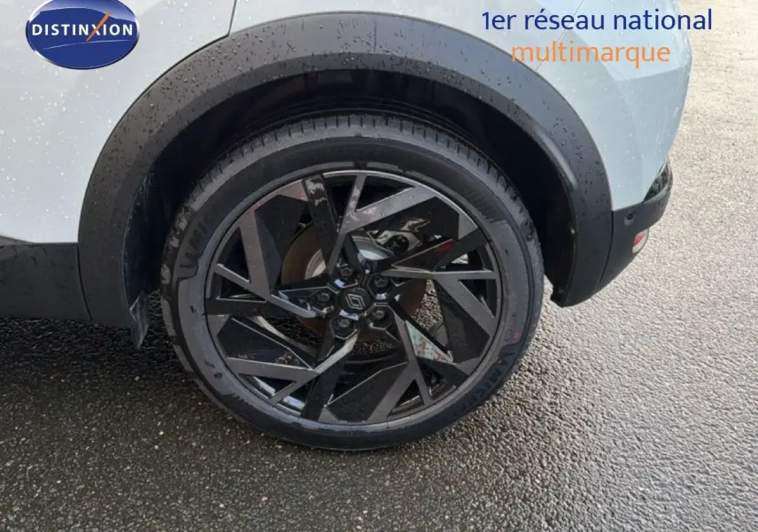 Gros plan sur la roue arrière droite d’un Renault Captur blanc nacré avec jante noire au design géométrique.