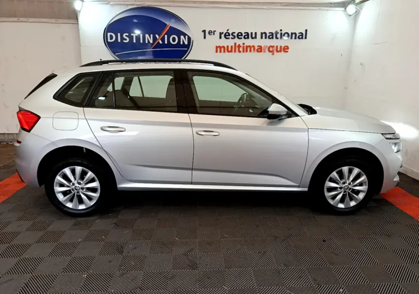 Vue latérale droite d'un Skoda Kamiq gris clair 2022 garé en intérieur avec rails de toit noirs visibles.