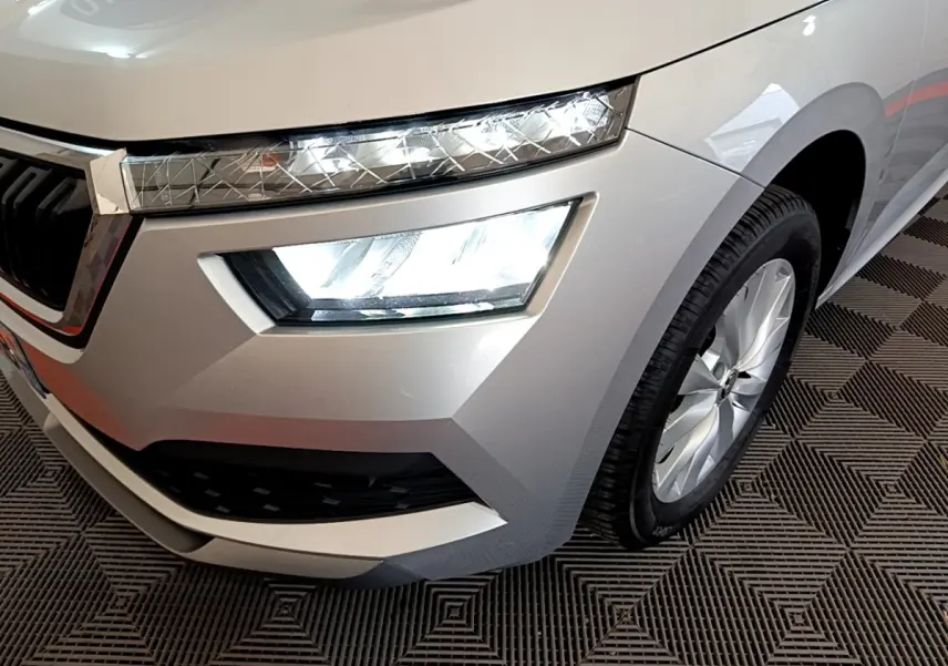 Gros plan sur l'avant droit gris clair du Skoda Kamiq 2022 avec phares LED allumés et jante alu visible.