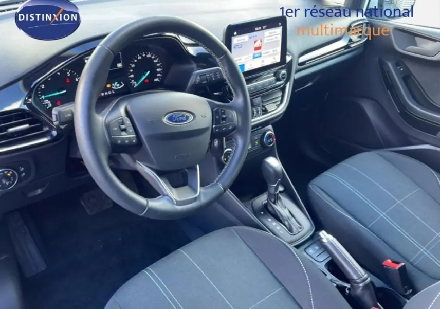 Vue intérieure avant droite de la Ford Fiesta 2020, montrant le volant, la console centrale avec écran tactile et la sellerie tissu noire.