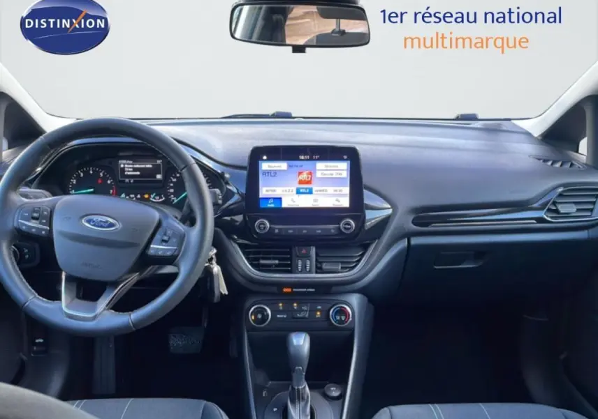 Vue intérieure avant centrée sur le tableau de bord et volant de la Ford Fiesta blanche avec écran tactile et boîte auto.