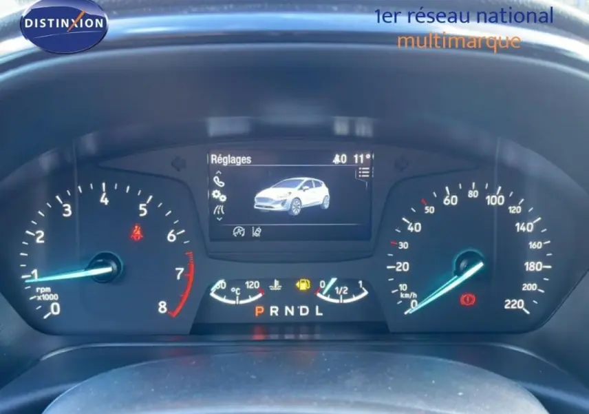 Vue rapprochée du tableau de bord numérique de la Ford Fiesta blanche, affichant les réglages et compteurs.