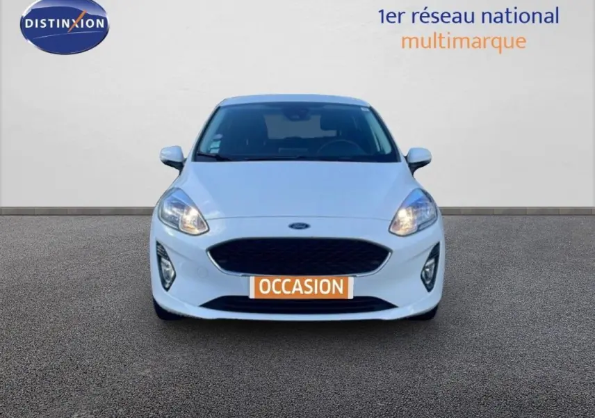 Vue frontale d'une Ford Fiesta blanche 2020 avec phares allumés et plaque "OCCASION" visible.