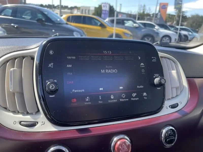 Vue rapprochée de l’écran multimédia tactile du tableau de bord d’une Fiat 500, avec commandes autour et intérieur bordeaux.